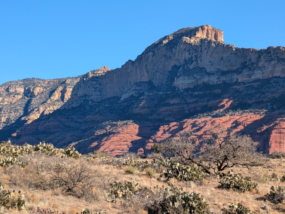 A side by side traversing a rugged, winding trail amidst the iconic red rock formations of Sedona, Arizona. The vehicle navigates the undulating terrain, kicking up a cloud of dust as it powers through the picturesque landscape. 