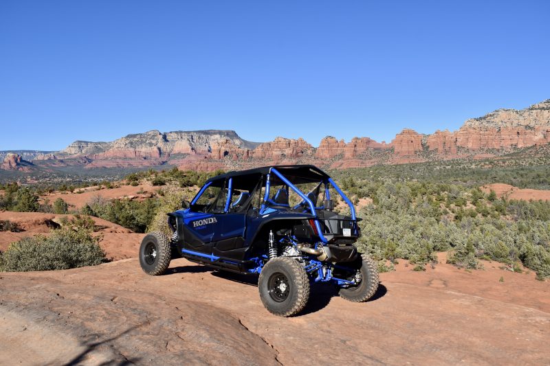 A rugged off-road vehicle navigating through the stunning red rock formations of Sedona, Arizona, with towering cliffs and unique sandstone spires in the background, vibrant blue sky, and scattered desert vegetation, capturing the spirit of adventure and exploration.