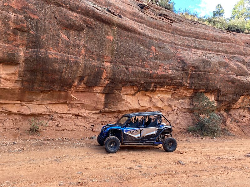 A thrilling off-road UTV traversing through the rugged, red rock landscape of Sedona, Arizona, with dramatic cliffs and vibrant desert vegetation in the background, showcasing a clear blue sky and brilliant sunlight illuminating the scene.