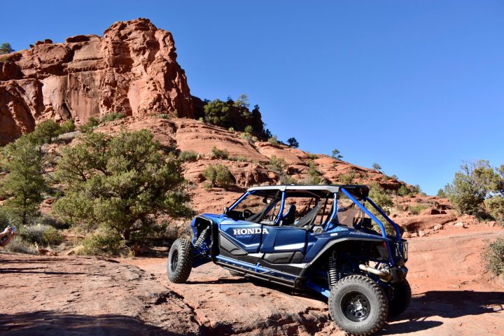 An off-road vehicle parked at the trailhead of a rugged Sedona landscape, surrounded by striking red rock formations and desert vegetation under a clear blue sky, showcasing the beauty of the outdoors and the adventure ahead.